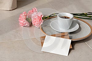 Blank paper card, postcard mockup, coffee cup, flowers on beige background in sun light, aesthetic holiday greeting or