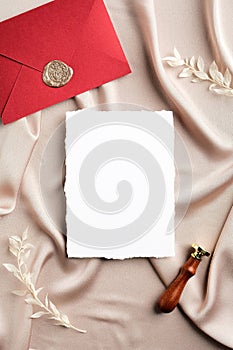 Blank paper card and red envelope with wax seal on silk fabric background. Flat lay, top view, copy space. Wedding invitation card