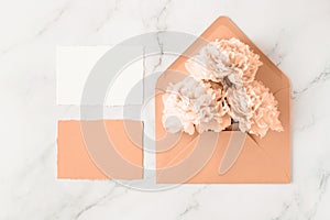 Blank paper cards and open retro peach fuzz envelope with peony flowers on white marble background