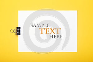 Blank paper with clamp on yellow background. Mockup with sample text for your design