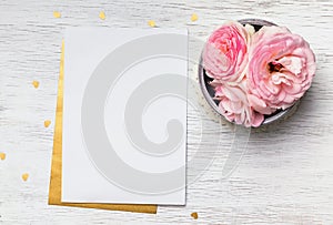 Blank paper and cute pink flowers on white wooden table