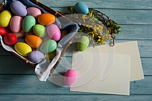 Blank paper, Forsythia branches and colorful Easter eggs on a light blue wooden background.