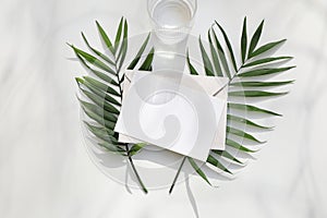 Blank paper, greeting card. Invitation mockup with fresh green palm leaves. Drinking lass with water in sunlight