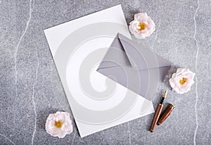 Blank paper, grey envelope, pen and roses on the gray background.Concept of wedding invitation template
