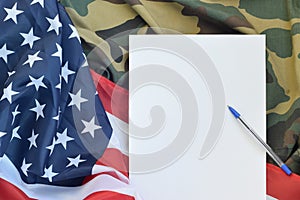 Blank paper lies on United States of America flag and folded military uniform jacket. Military symbols conceptual background