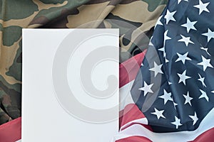 Blank paper lies on United States of America flag and folded military uniform jacket. Military symbols conceptual background