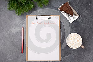 Blank paper with new year`s resolutions title, coffee, bar of chocolate and red pencil on grey table. Flat lay. Top view