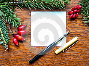 Blank paper note with pen and Christmas tree branches on wooden