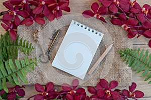 Blank paper note, pencil and vintage key on wooden table decorated with red orchid and green fern
