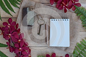 Blank paper note, pencil and vintage key on wooden table decorated with red orchid and green fern