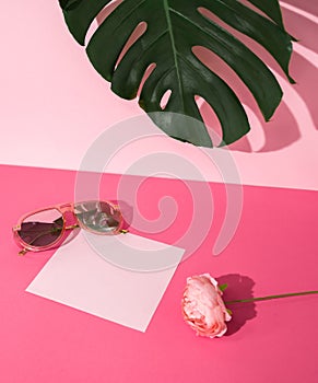 Blank paper note, woman sunglasses and a flower on bright pink background