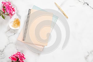 Blank paper notebook, pink flowers, golden stationery on marble background. Flat lay, top view feminine home office desk