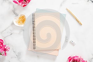 Blank paper notebook, pink flowers and golden stationery on marble background. Flat lay, top view modern home office desk. Fashion