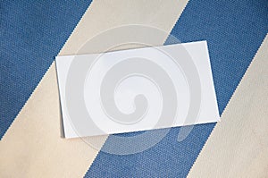 Blank paper person card lying on striped fabric. Topp view, copy space for text