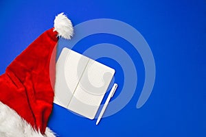 Blank paper sheet and Snata Claus hat on blue background