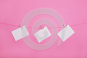 Blank paper sheets on a clothes line on a pink background. Pink hearts on clothespegs. Valentines day, Mother Day concept.
