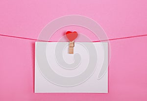 Blank paper sheets on a clothes line on a pink background. Red hearts on clothespegs. Valentines day, Mother Day concept.