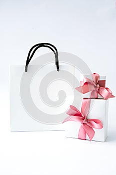 Blank paper white bag and two gift present boxes with pink ribbon on white background. Black friday sale. Shopping