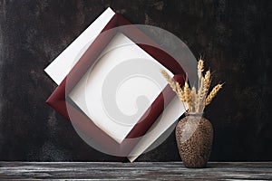 Blank paper and wooden frame mock up with ears of ripe wheat in a modern vase. Vintage wooden table and dark brown grunge backdrop