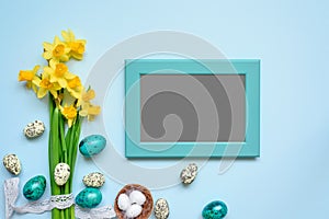 Blank photo frame with easter eggs and spring flowers mock up over blue background. top view