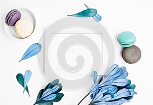 Blank photo frame mockup with macarons and blue leaves