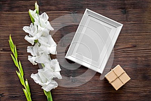 Blank photo frame near flower gladiolus on dark wooden background top view mockup