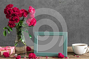 Blank photo frame and rose flowers with cup of tea and gift box on rustic wooden table. mock up. still life