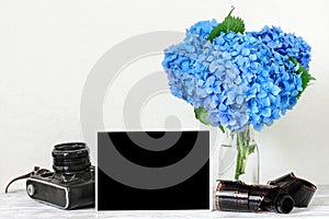 Blank photo frame and vintage retro camera with beautiful bouquet of blue hydrangea flowers and rolled film