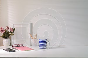Blank picture frame, coffee cup, notebook and flower pot on white table. Copy space for your text
