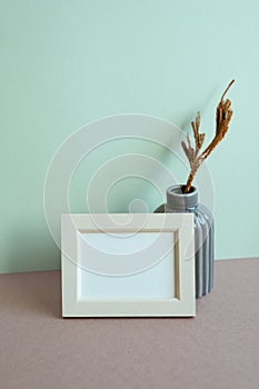 Blank picture frame and vase of dry plant on table. mint wall background. copy space