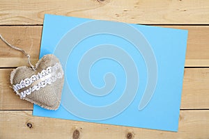 Blank piece of paper and vintage handmade valentines day toy heart over wooden background