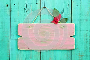 Blank pink weathered sign with red flower hanging on antique green wood door