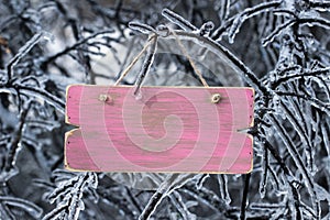 Blank pink wooden sign with ice covered tree branches