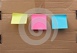 Blank pink, yellow and blue square papers  glued on a brown cardboard surface