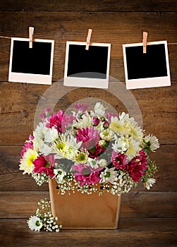 Blank polaroid photo frames hanging on a rope with summer bouquet of pink and white flowers on wooden table with wooden background