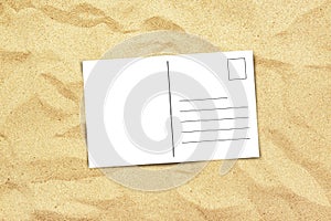 Blank postcard on beach sand, top view