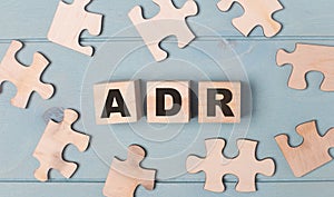 Blank puzzles and wooden cubes with the text ADR Alternative Dispute Resolution lie on a light blue background