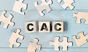 Blank puzzles and wooden cubes with the text CAC Customer Acquisition Cost lie on a light blue background