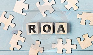 Blank puzzles and wooden cubes with the text ROA Return On Assets lie on a light blue background