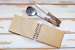 Blank recipe book and knife and spoon with wooden handle, top view. blank notepad for recipe on white board table. Place for text