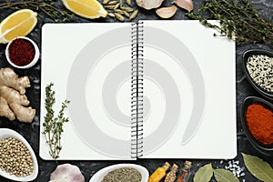 Blank recipe book surrounded by different ingredients on black textured table, flat lay. Space for text