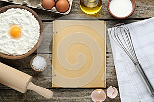 Blank recipe book surrounded by different ingredients on wooden table, flat lay. Space for text