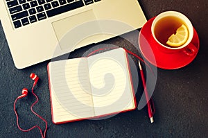 Blank red notebook, computer laptop, headphones and cup of tea