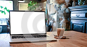 Blank screen laptop and coffee cup putting together on the wooden table with the beautiful classic decorate room as background.