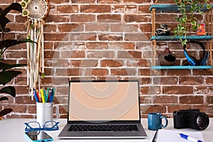 Blank screen laptop computer in office room with accessories and decorations, copy space. Brick wall background