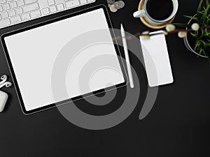 Blank screen smartphone, tablet, other supplies, decorations and copy space on dark modern worktable