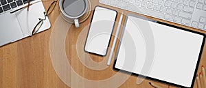 Blank screen smartphone and tablet on wooden office desk with coffee cup, supplies and copy space