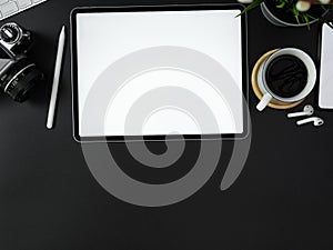 Blank screen tablet, camera, coffee cup, other digital devices and decoration on dark modern office desk