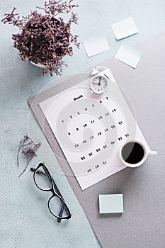 Blank sheet of monthly calendar, glasses, coffee cup and alarm clock on the desktop. Time planning and organization. Vertical view