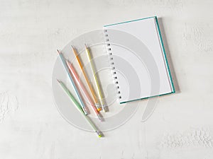 Blank sheet notebook with copy space for text and multicolored graphite pencils on white background. Flat lay, top view girl work